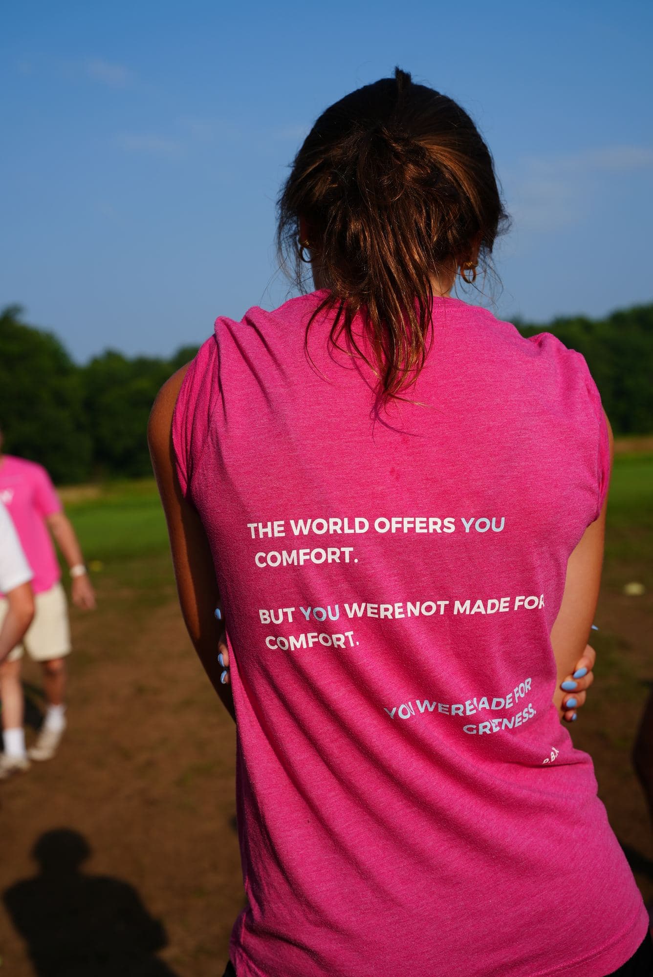 The pink tee from behind under a clear sky, the manifesto legible across the back