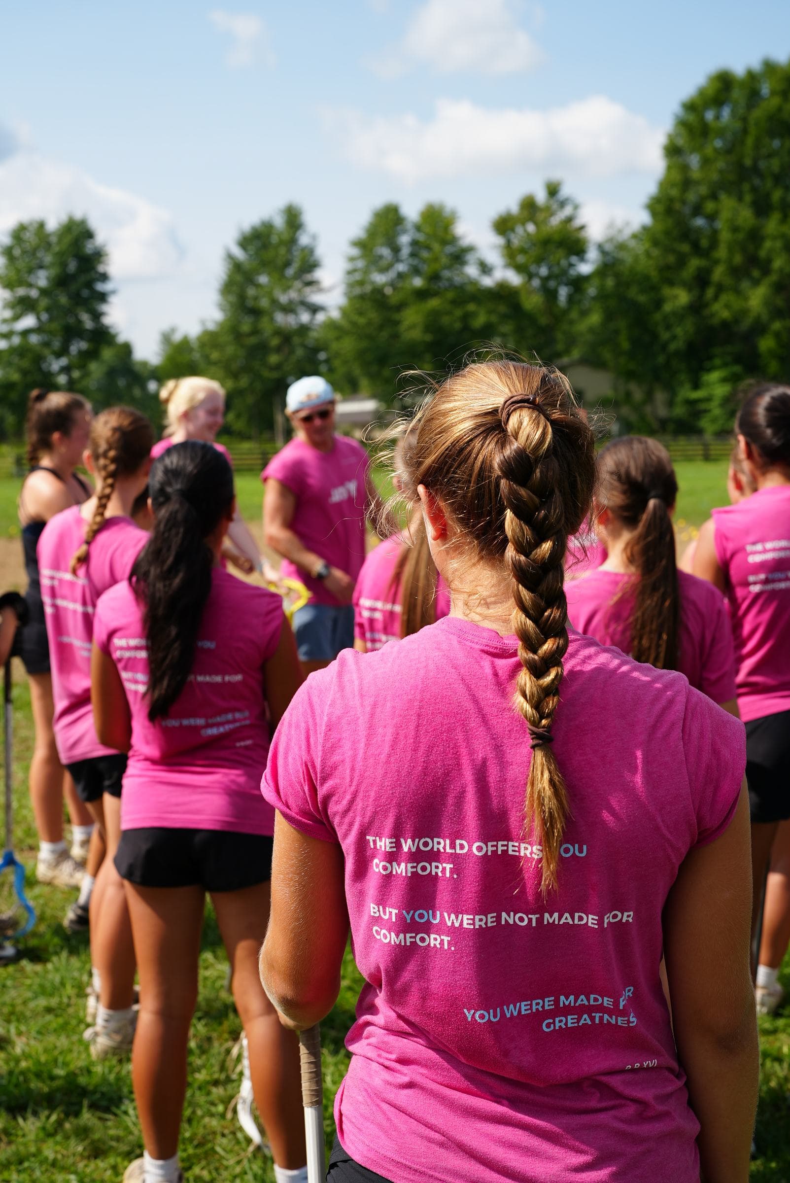 A full team in the pink tee, backs turned, the manifesto repeating down the line at a summer session