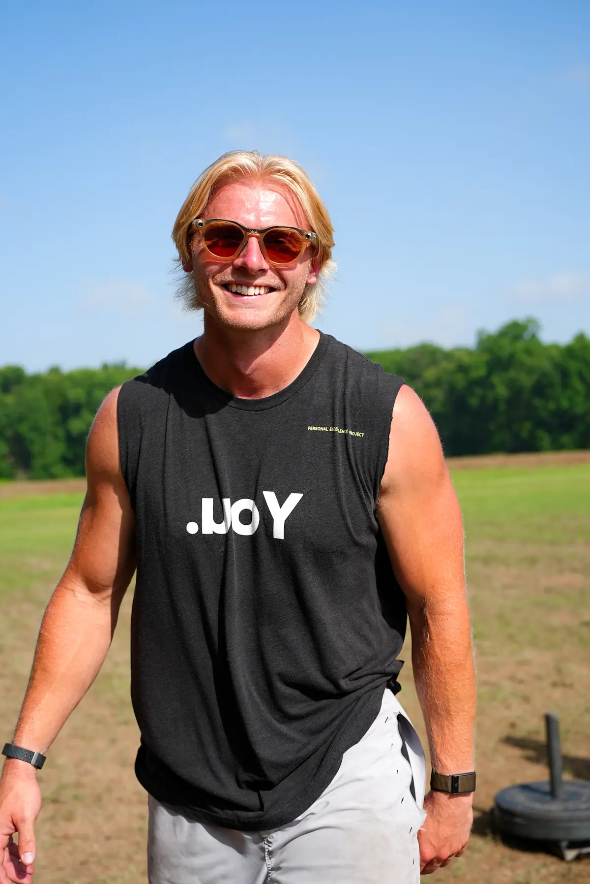 Harrison Schertzinger smiling on the field in a sleeveless .uoY shirt and sunglasses