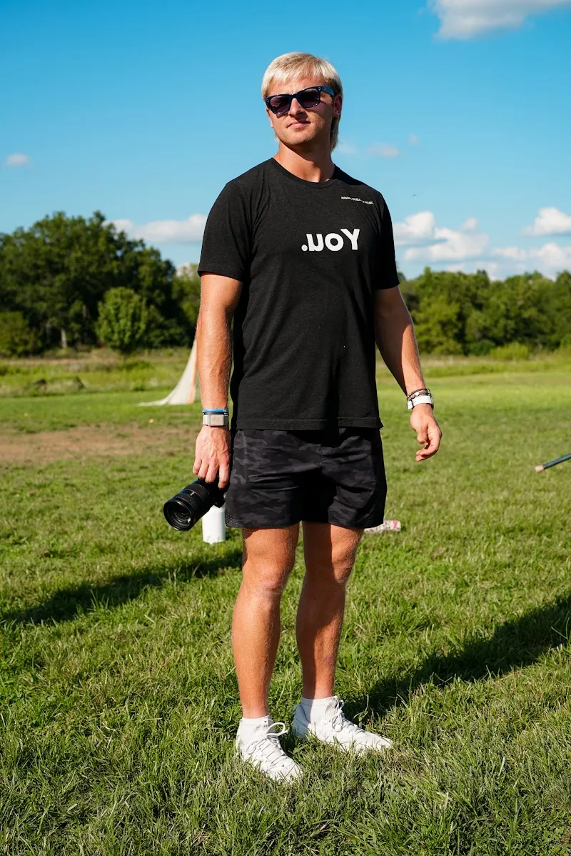 Henry Schertzinger standing on the field in a black .uoY tee, camera in hand